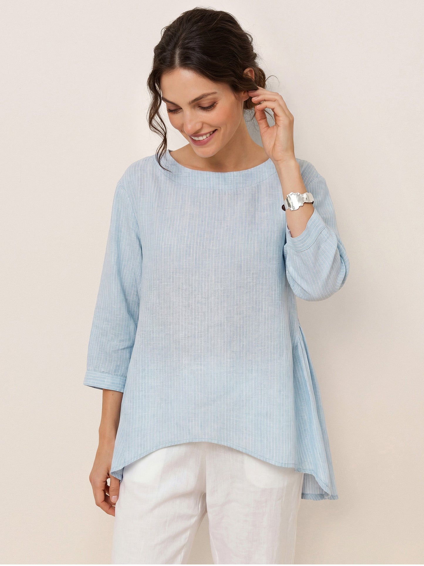 Woman wearing a light blue ribbed sweater with white pants on a beige background