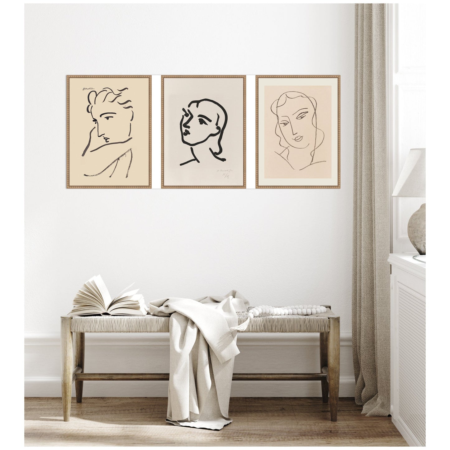 Three framed line art portraits on a wall above a bench with an open book and white blanket.