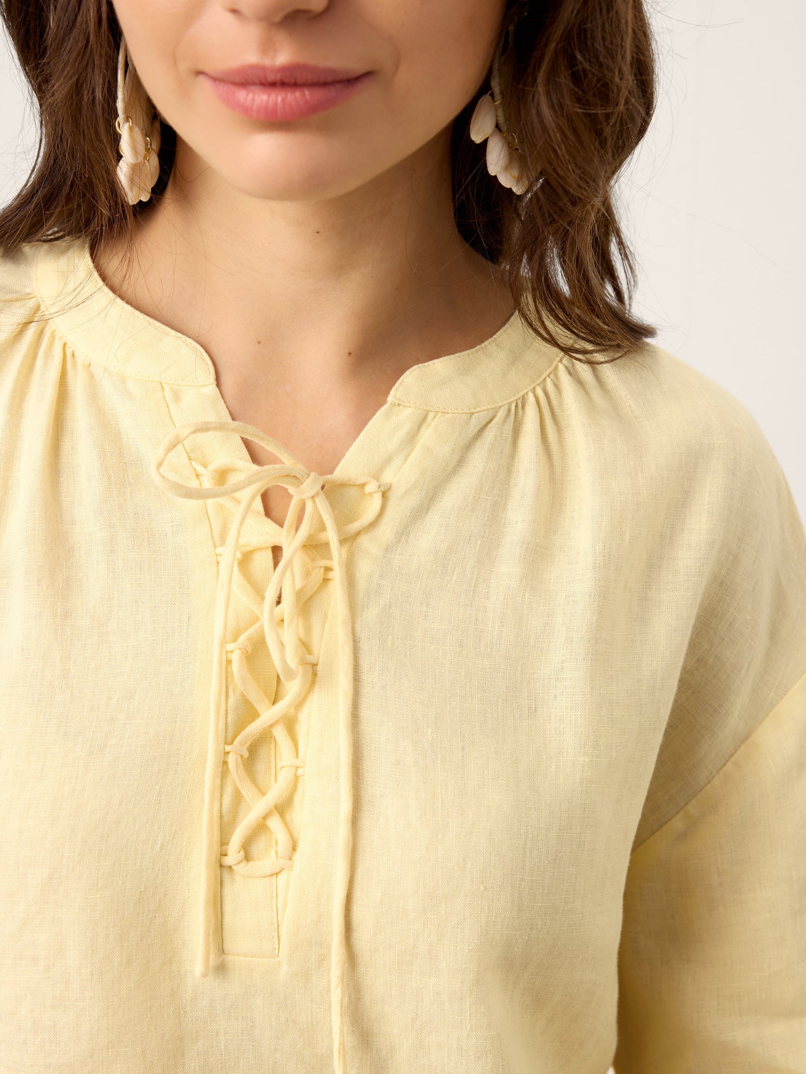 Close-up of a person wearing a light yellow blouse with lace details on a white background