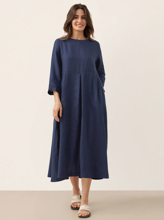 A woman modeling a navy blue midi dress with three-quarter sleeves and a relaxed, loose fit, standing against a solid beige studio background.