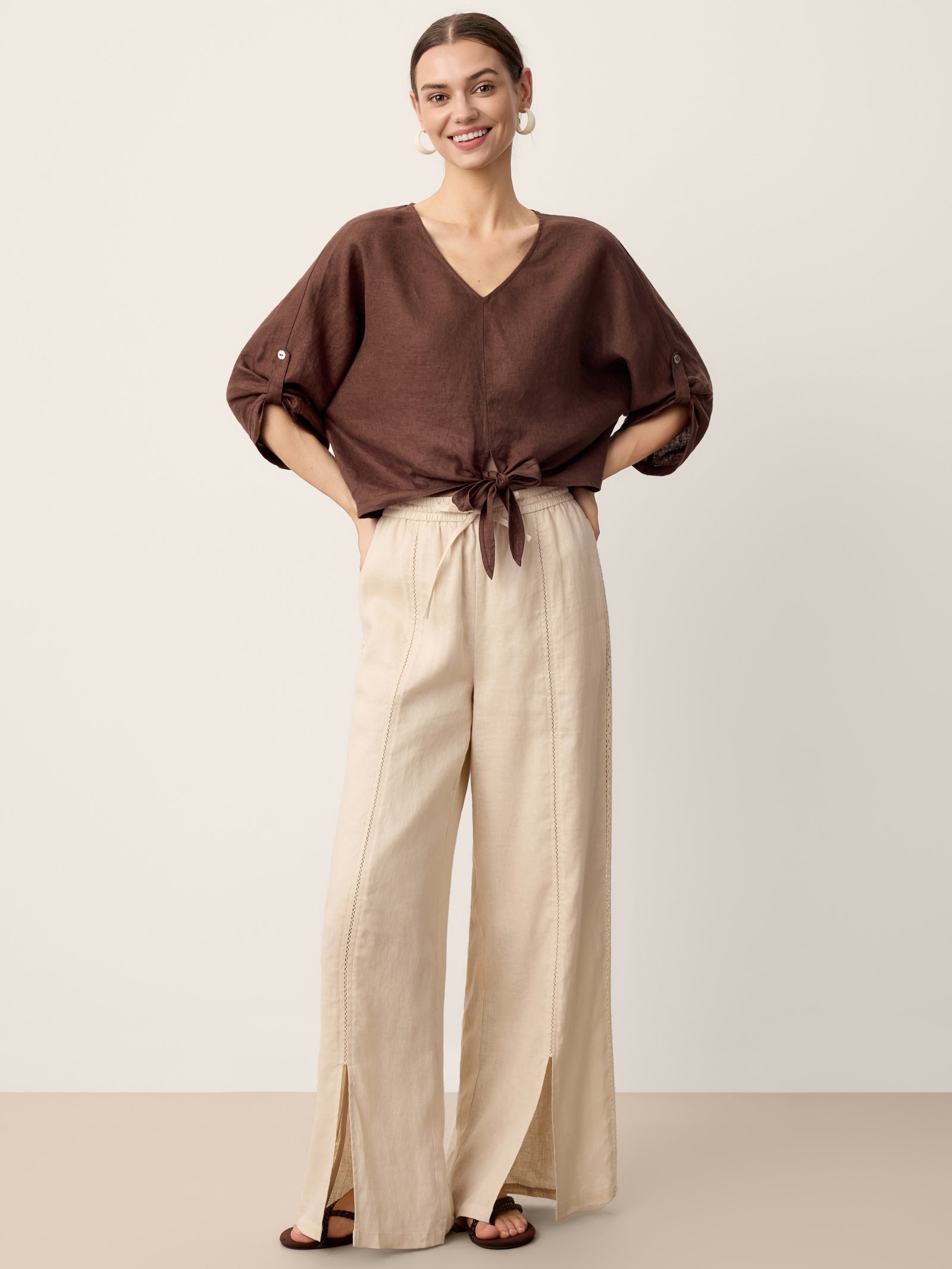 Woman wearing a brown blouse and beige wide-leg pants on a plain background
