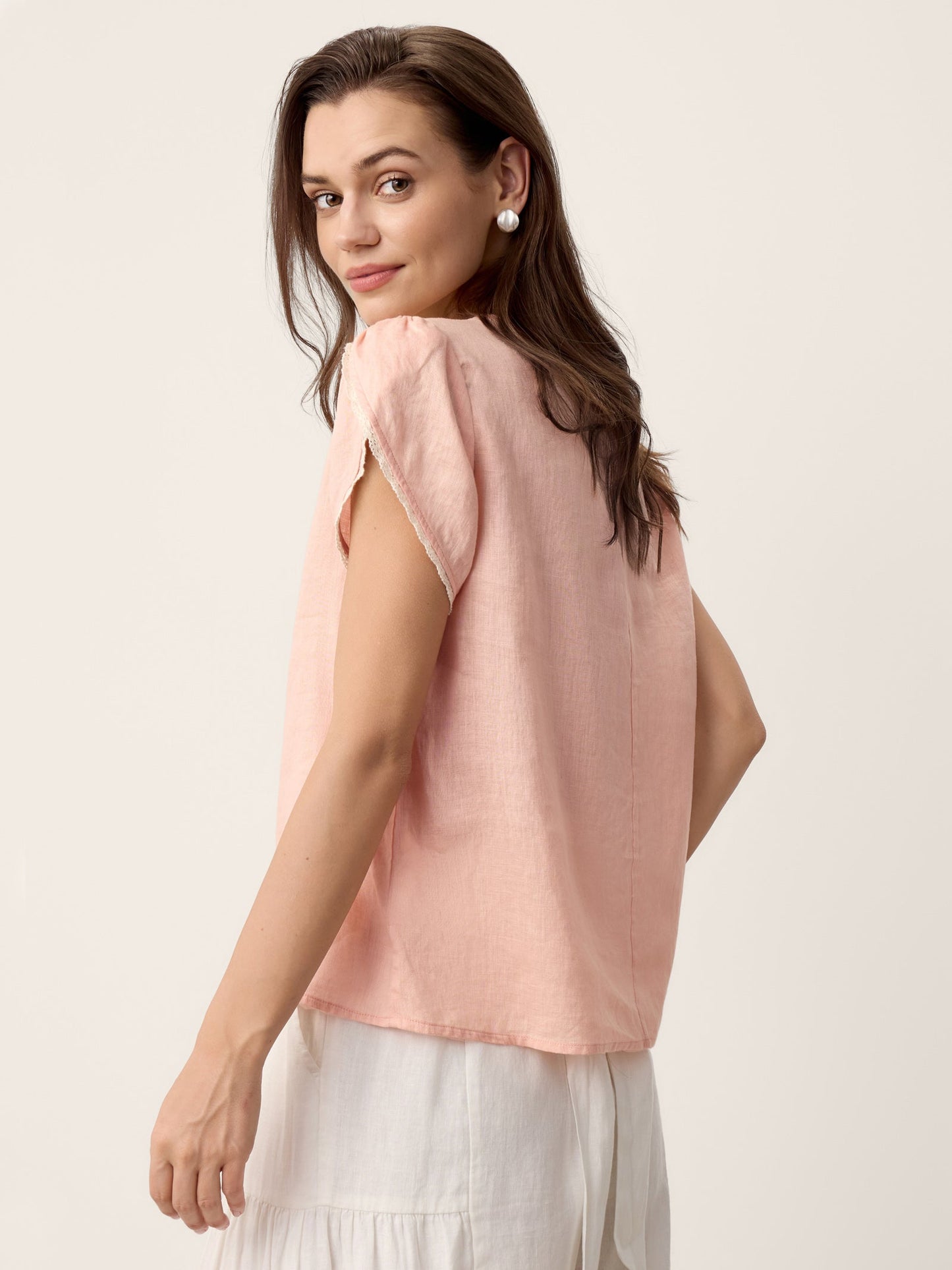 Woman wearing a light pink sleeveless top with a plain background
