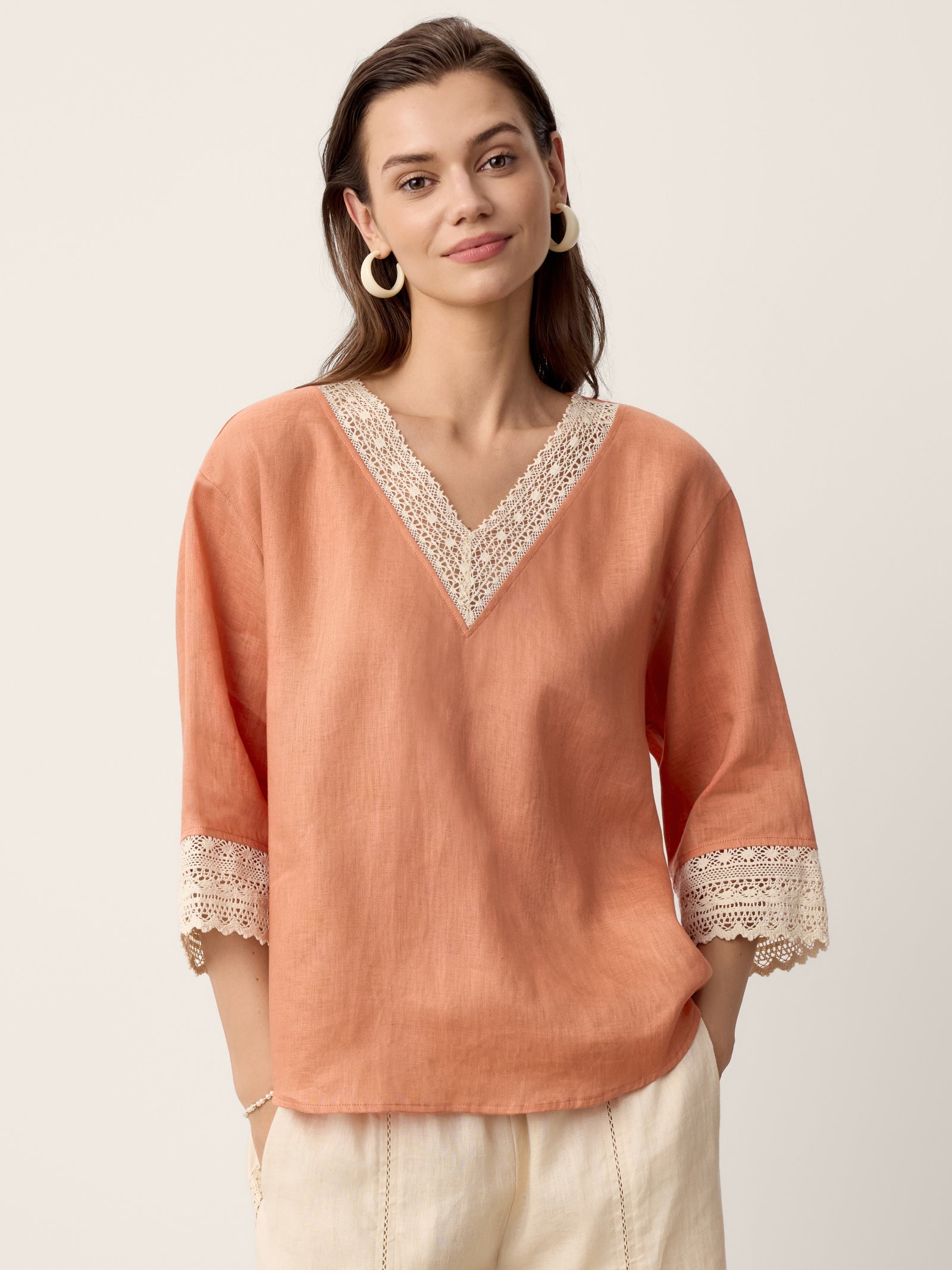 Woman wearing a peach-colored blouse with lace details on a plain background