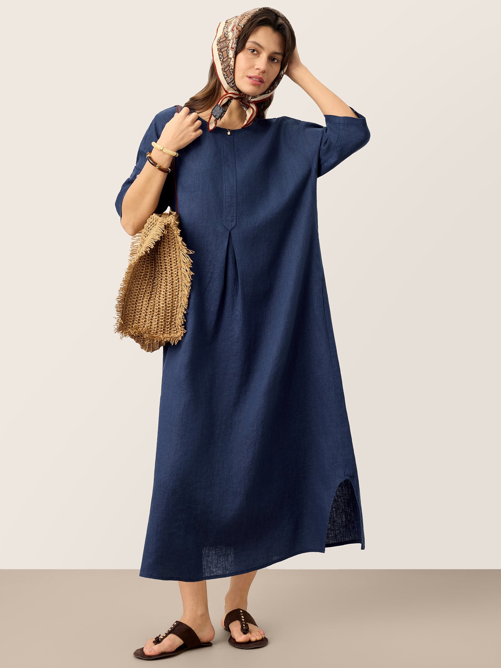 Woman wearing a blue dress holding a woven bag against a plain background
