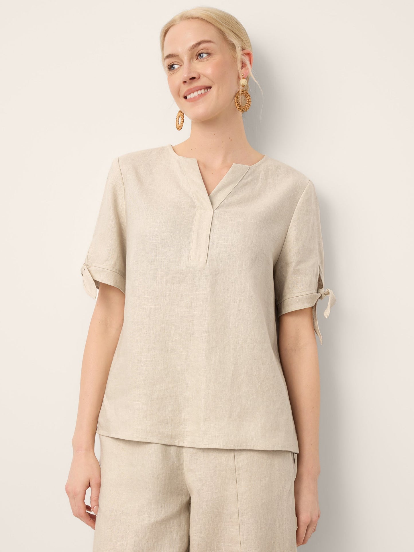 Woman wearing a beige top and pants against a white background