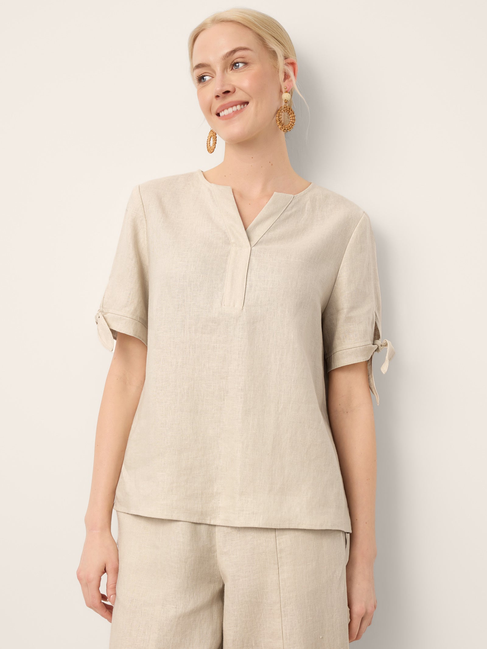 Woman wearing a beige top and pants against a white background