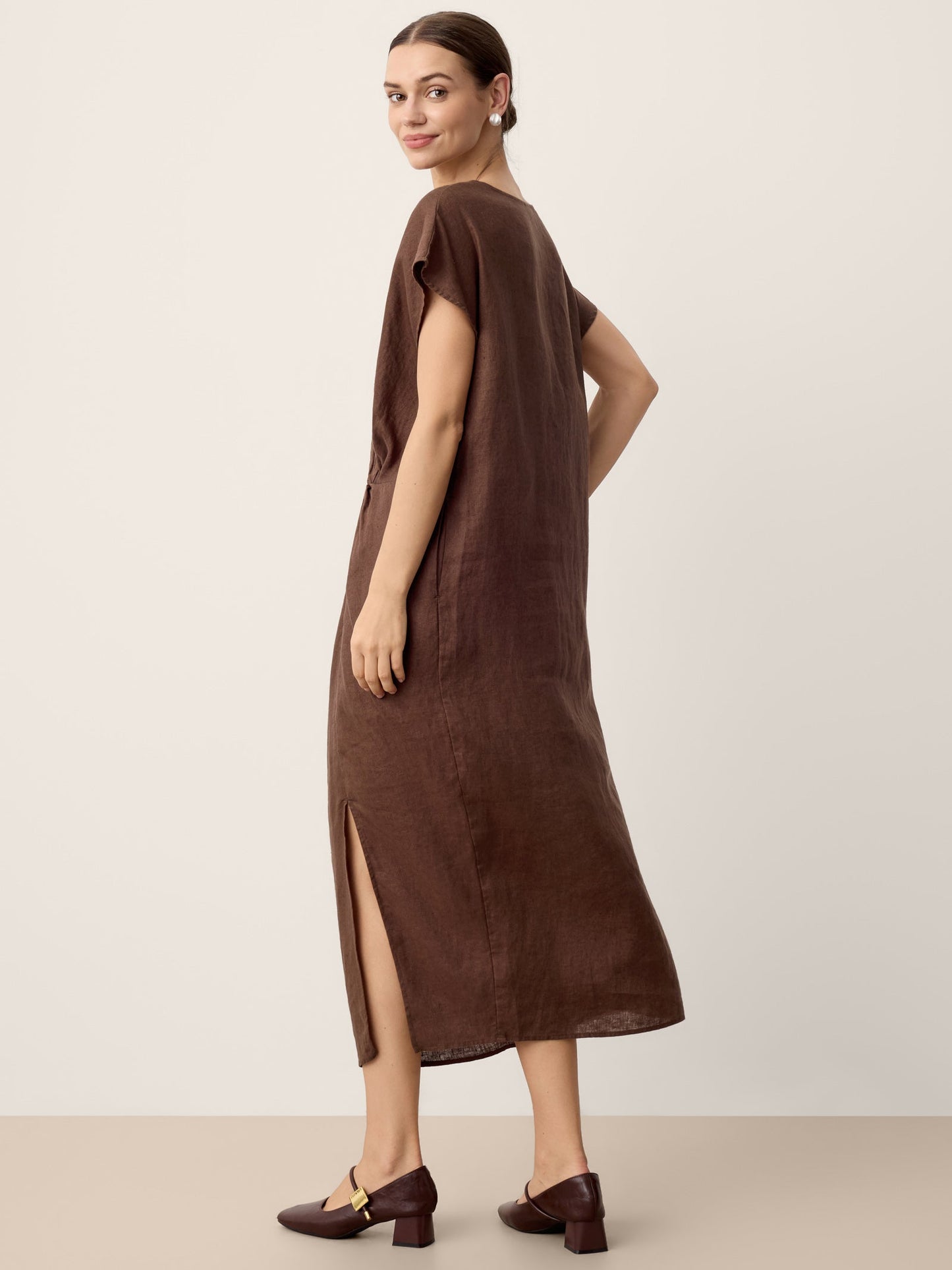 Woman wearing a brown dress with a slit on a plain background