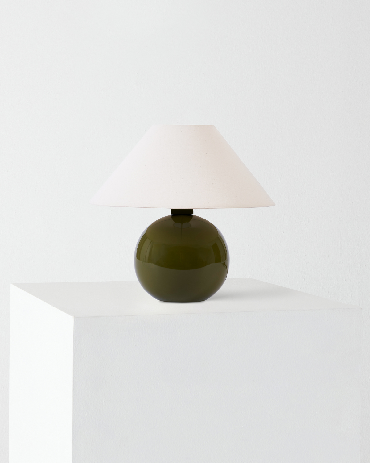 Table lamp with a green base and white shade on a white surface.