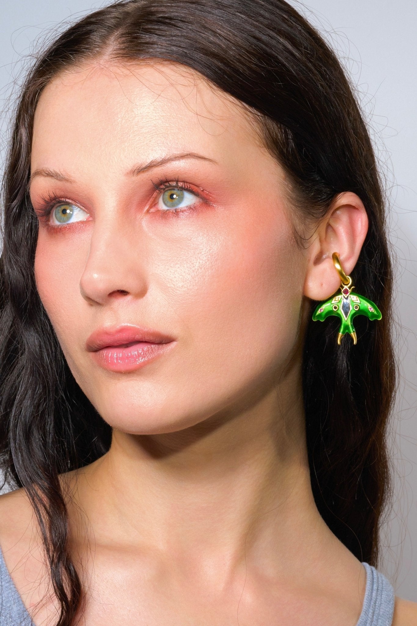 Close-up of a woman wearing a green and gold earring against a neutral background
