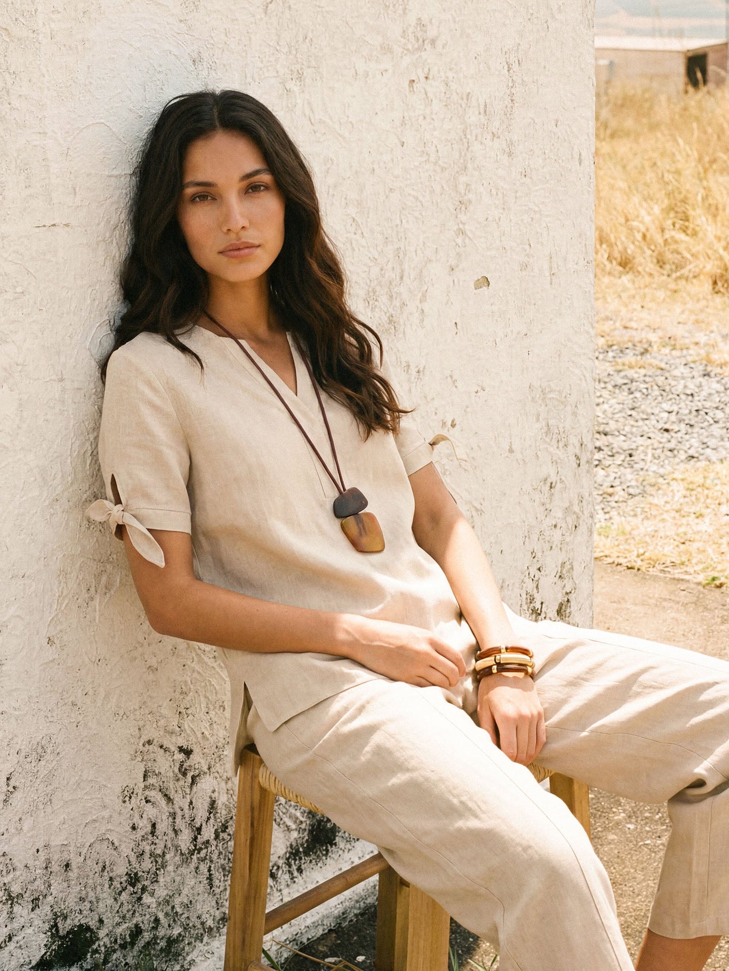 Woman in a beige outfit sitting on a chair against a textured wall.