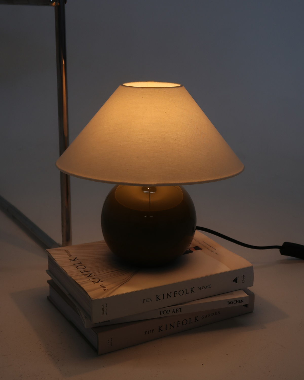 Small lamp with a beige shade on top of books in a dimly lit room