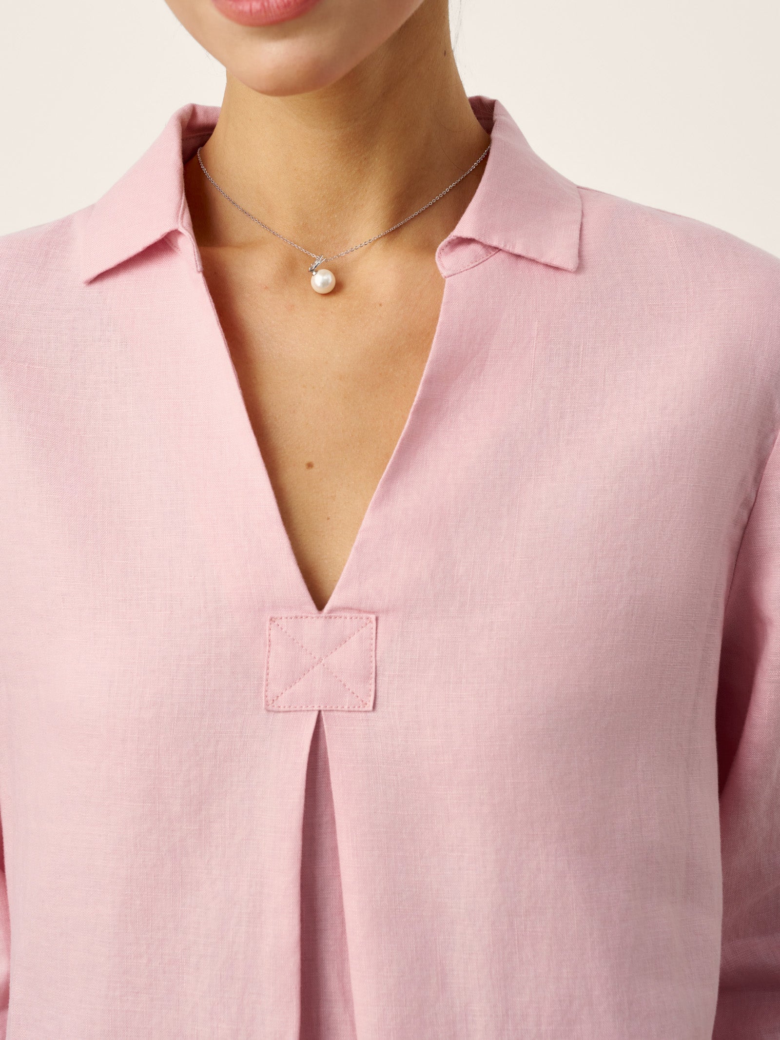 Close-up of a person wearing a pink blouse with a necklace.
