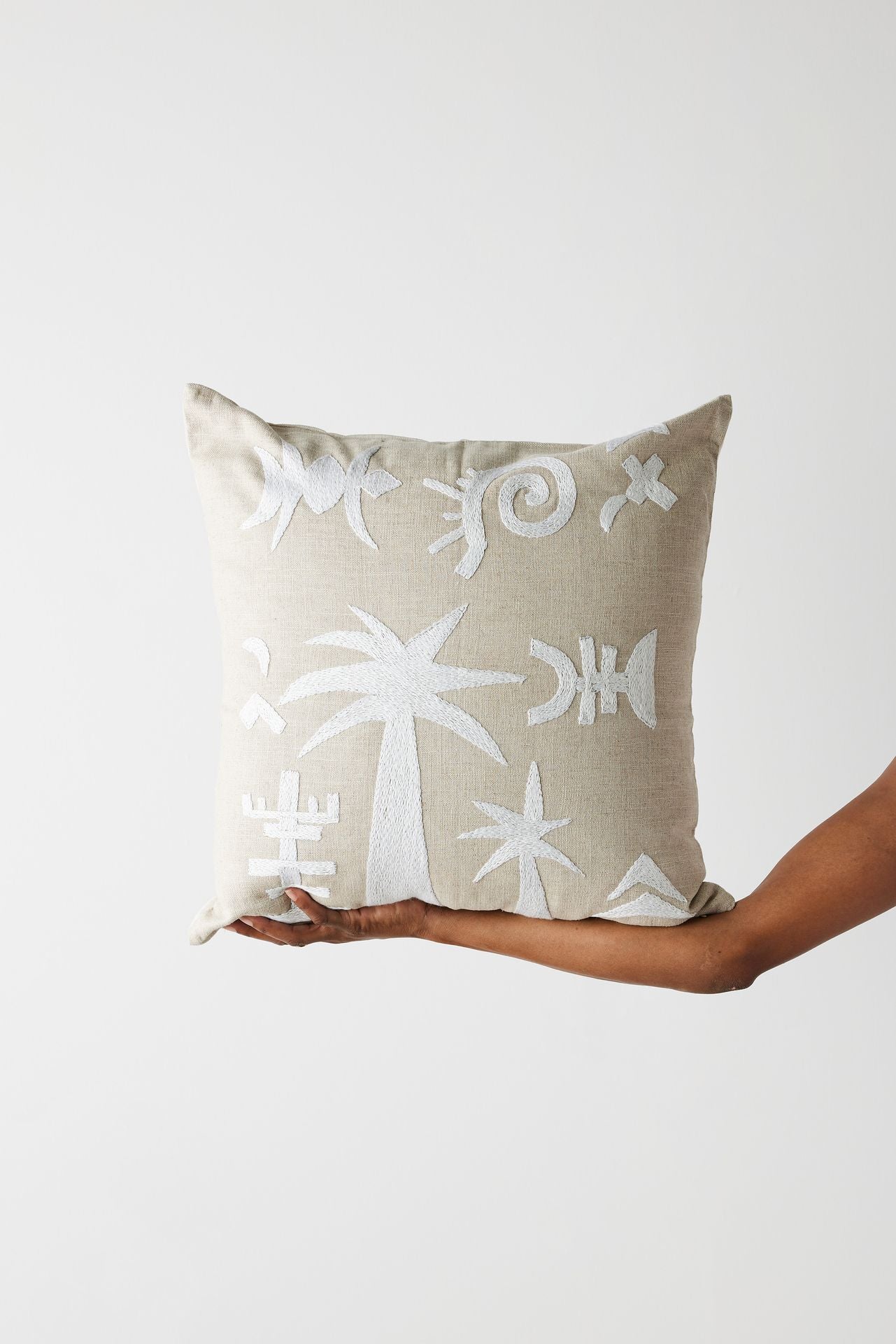 Beige pillow with white patterns held by a hand against a light gray background
