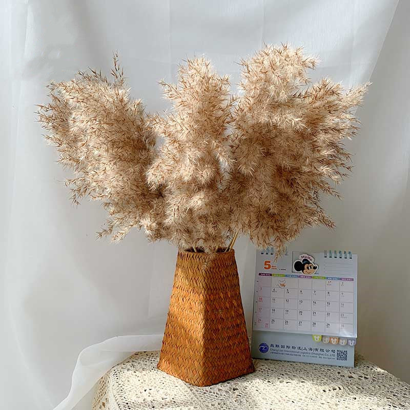 Dried pampas grass in a woven vase on a surface with a calendar in the background.