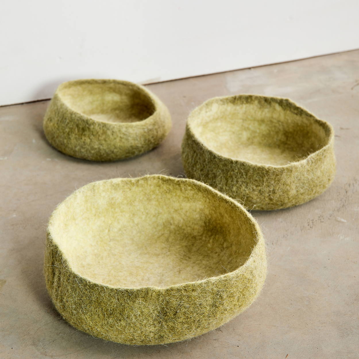 Three green woven bowls on a concrete surface