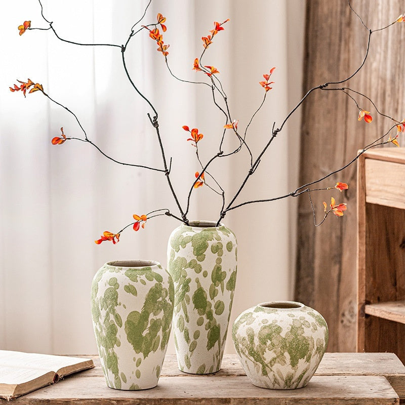 Three green and white patterned vases with branches and orange flowers on a wooden surface.