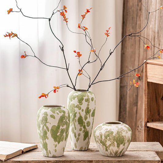 Three green and white patterned vases with branches and orange flowers on a wooden surface.