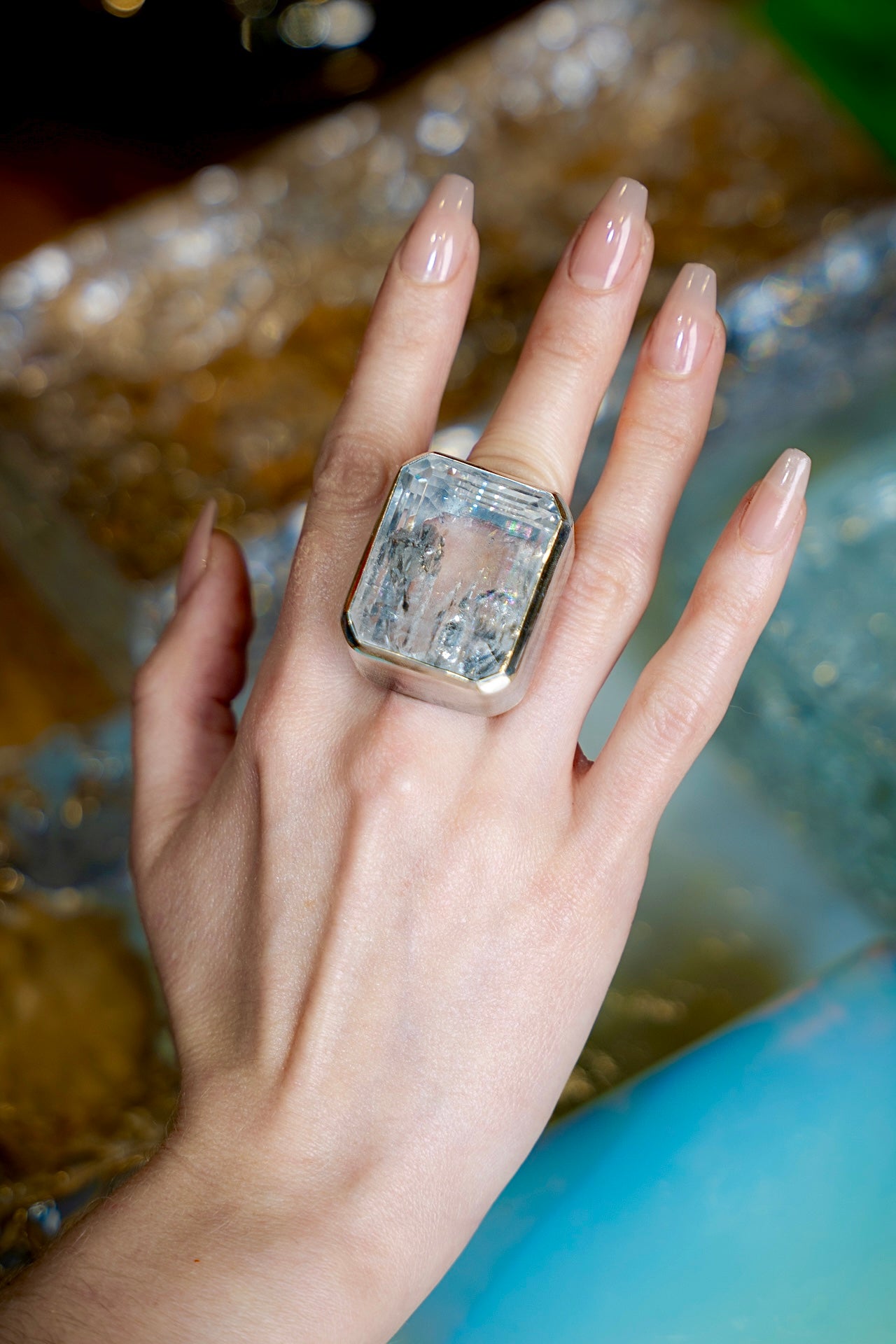 Hand wearing a large diamond ring with a blurred background