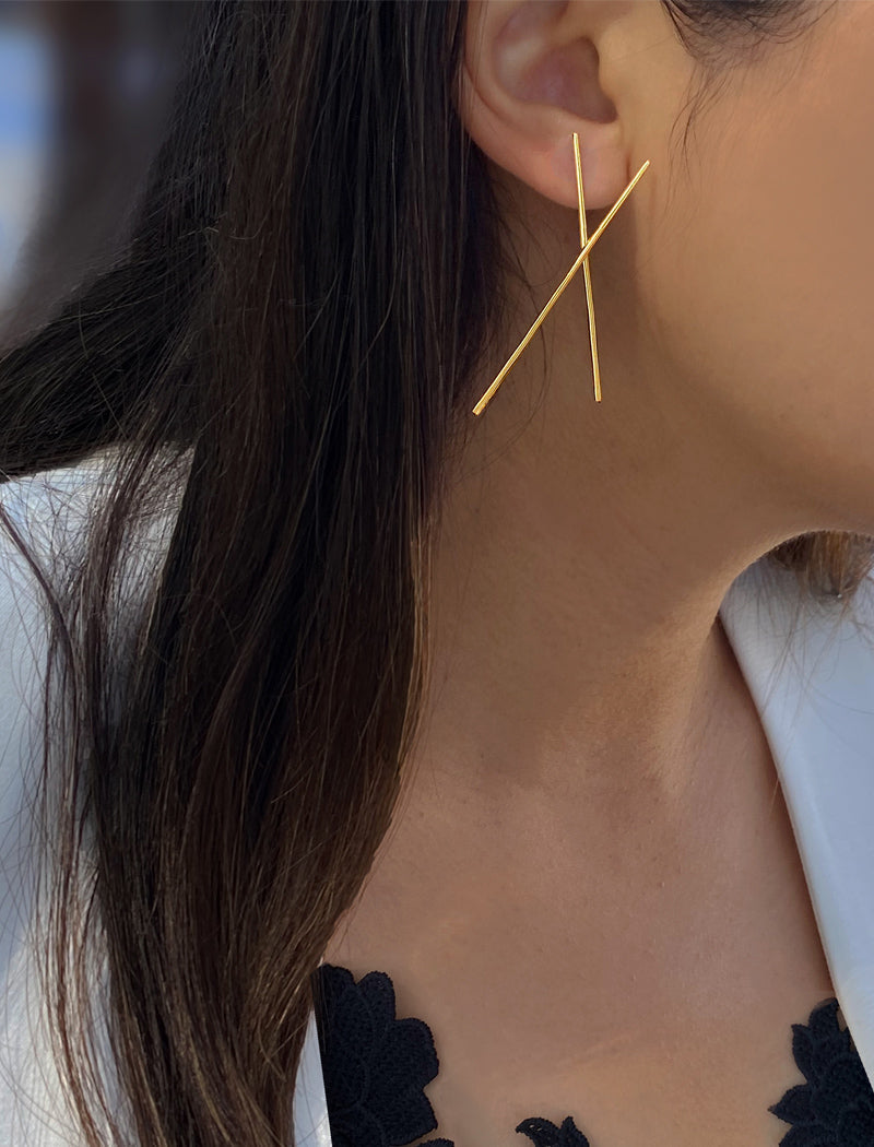 Close-up of a person wearing a gold 'X' shaped earring.
