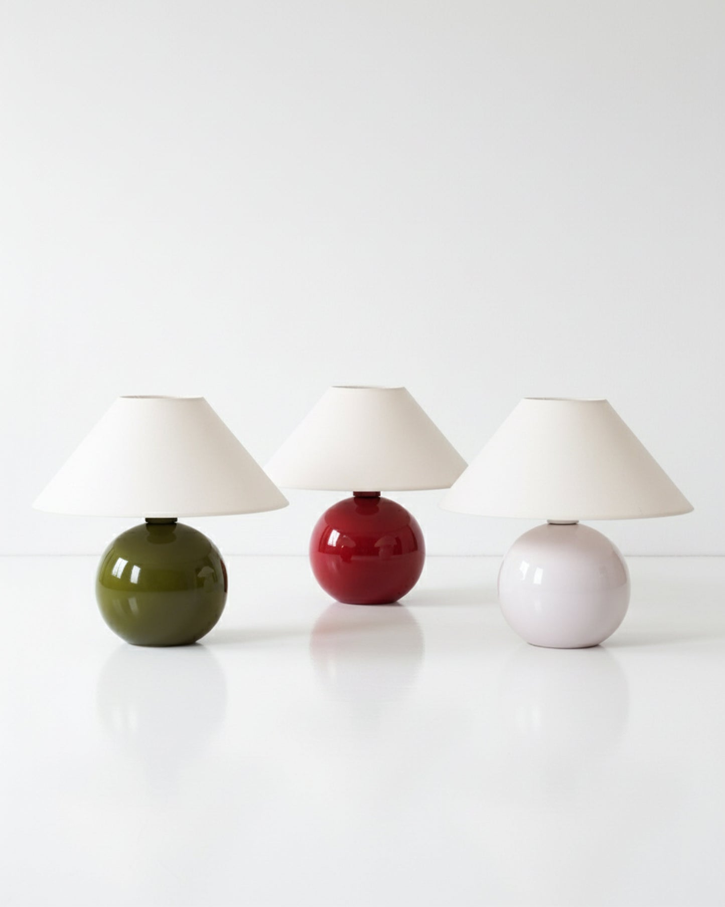 Three ceramic table lamps with different colored bases on a white surface.