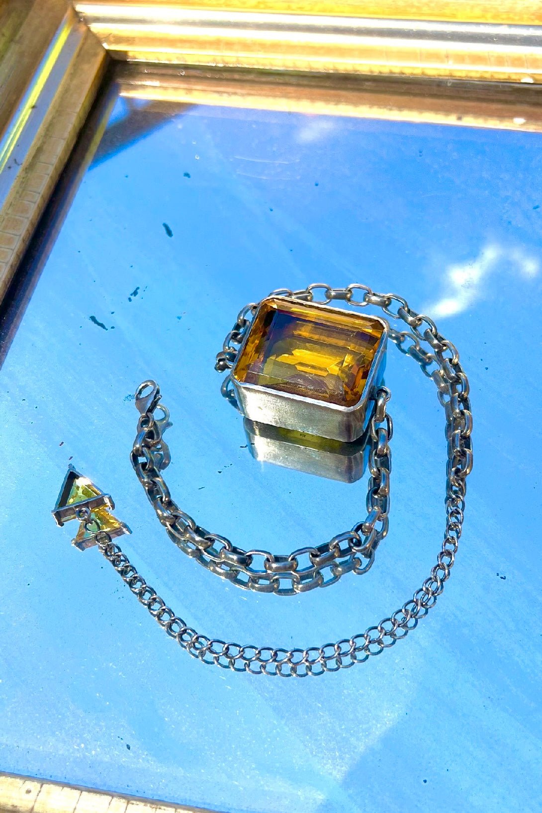 Silver chain necklace with a rectangular pendant on a reflective surface