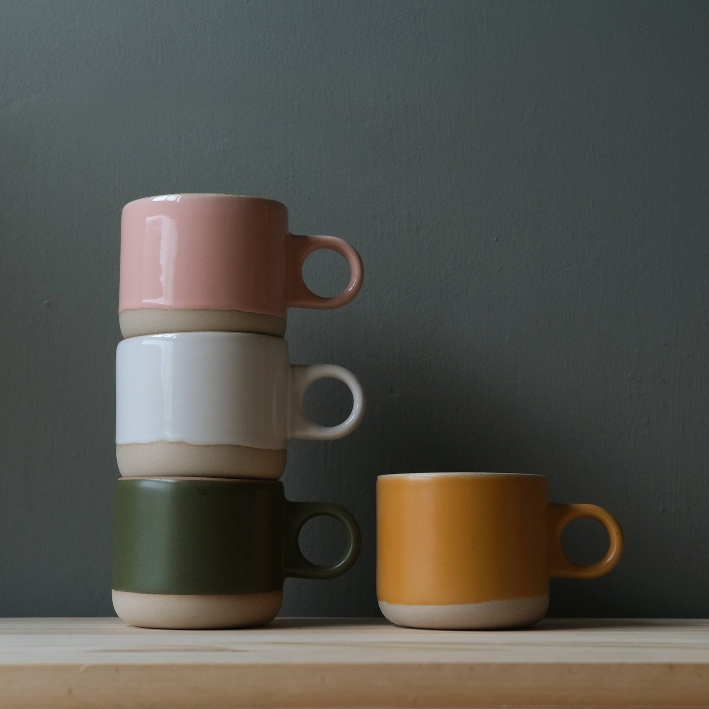 Four colorful mugs stacked and placed on a wooden surface with a dark gray background