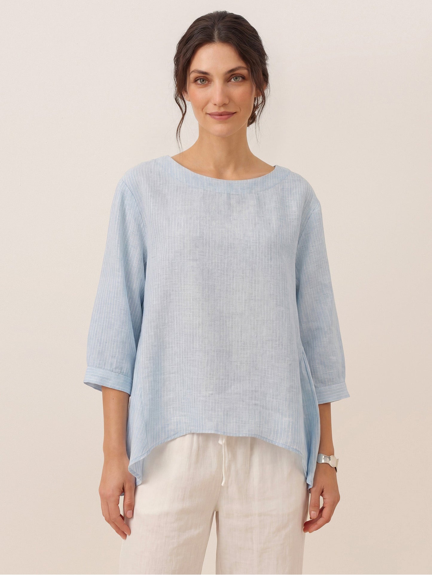 Woman wearing a light blue sweater over a white shirt with beige pants on a plain background