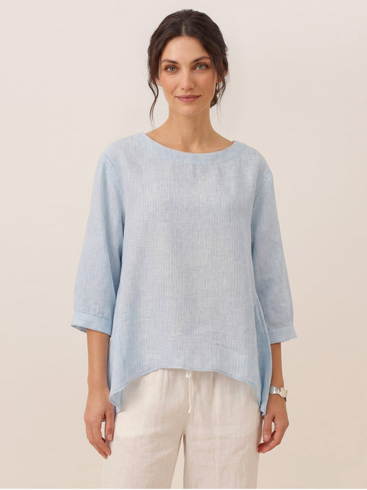 Woman wearing a light blue sweater over a white shirt with beige pants on a plain background