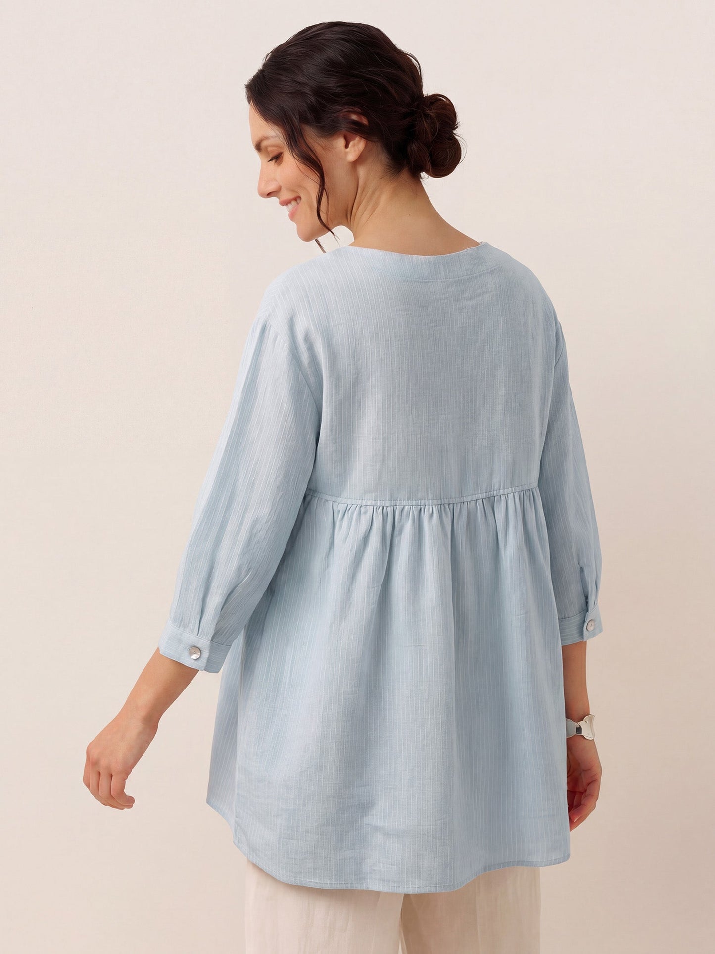 Woman wearing a light blue tunic with a plain background