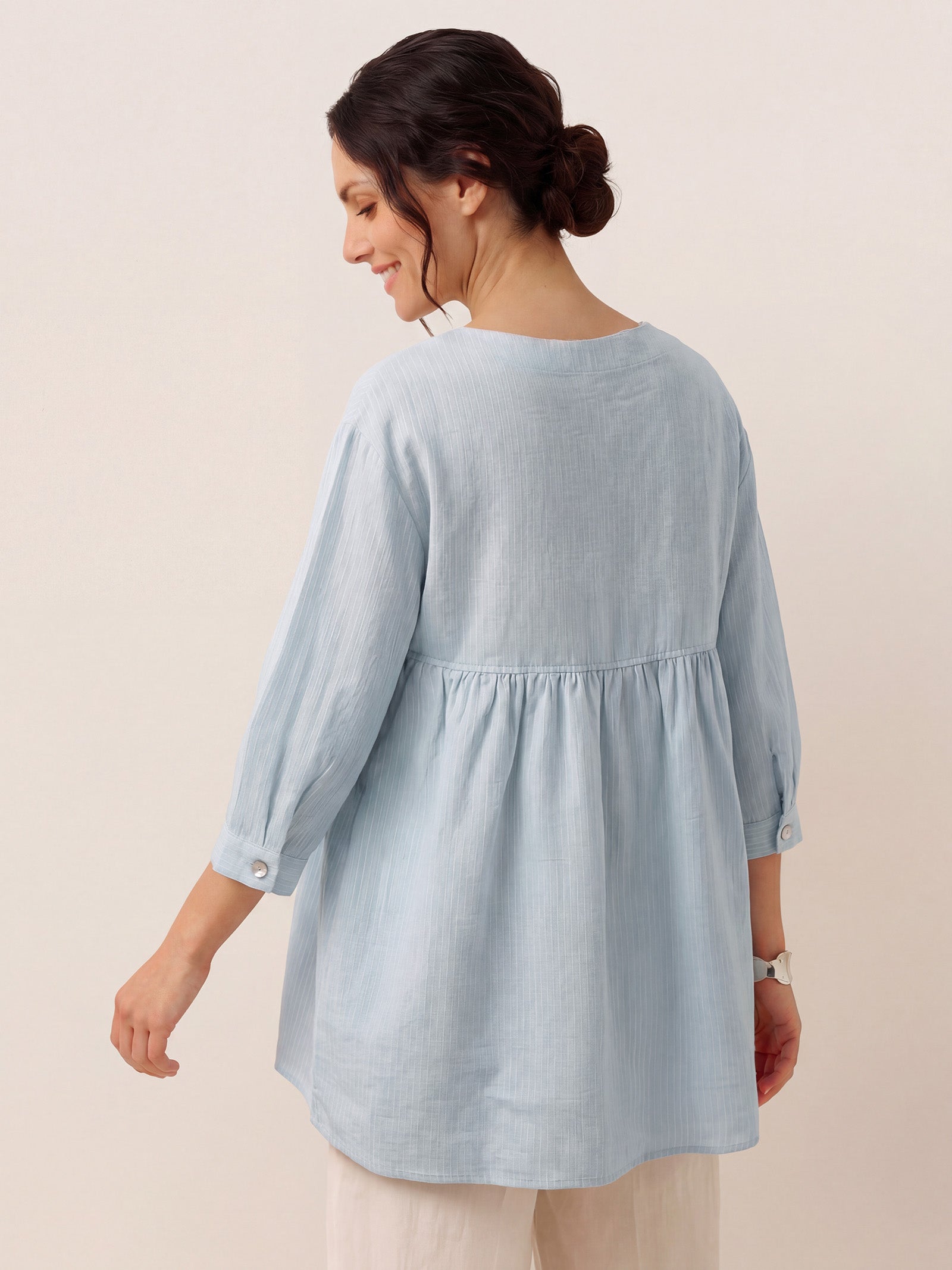 Woman wearing a light blue tunic with a plain background