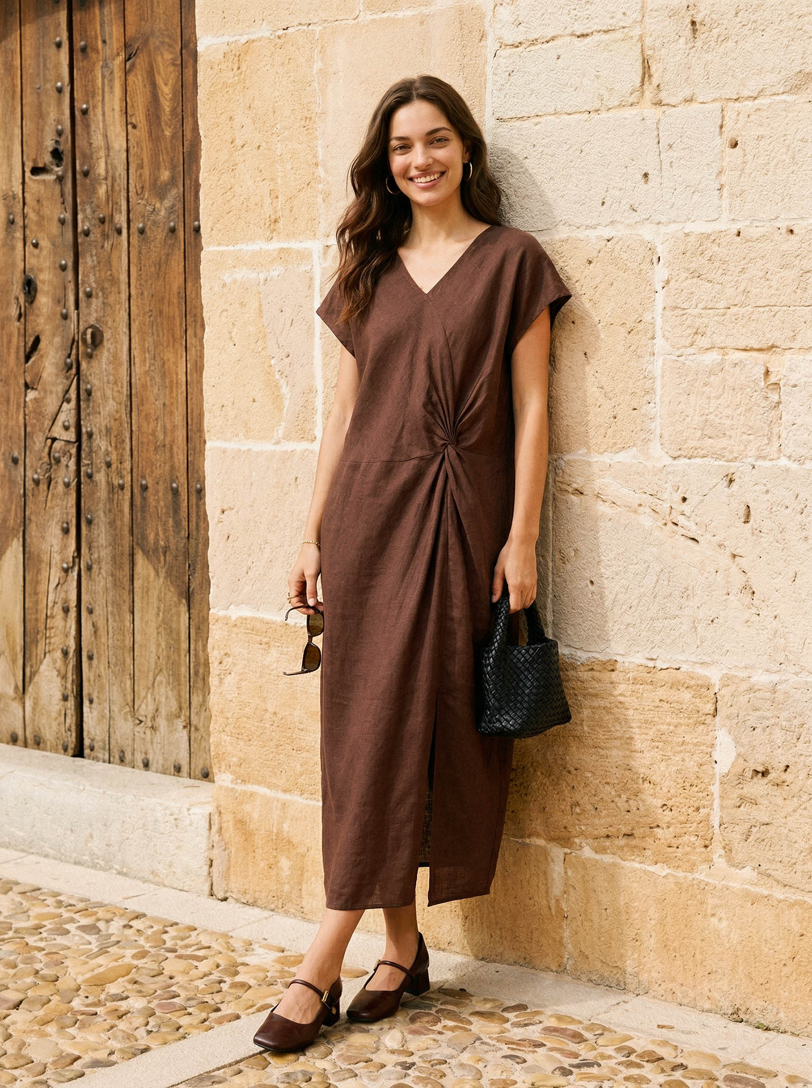 Woman in a brown dress standing against a stone wall.