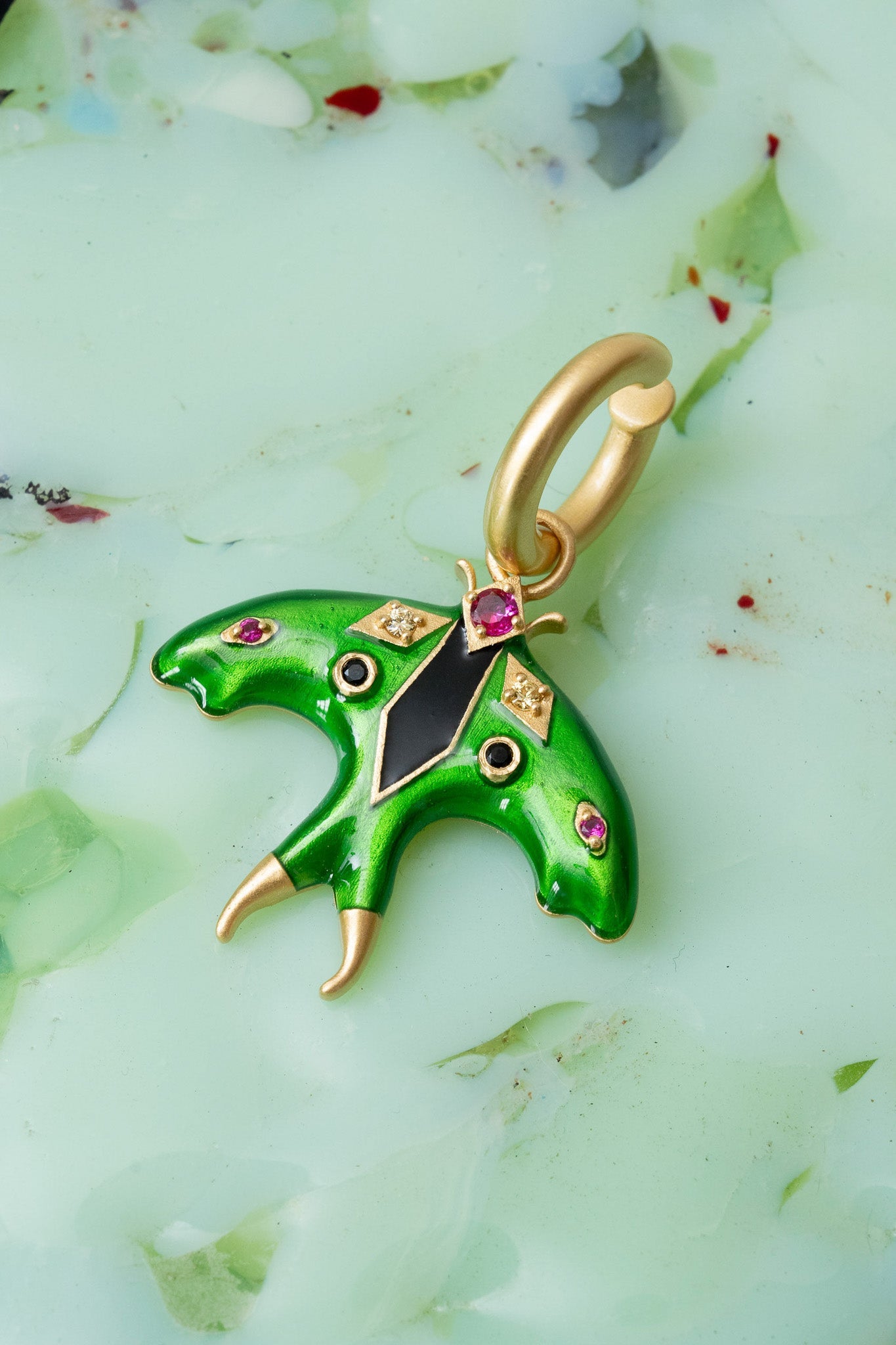 Green butterfly pendant with gold and gemstone accents on a light green background