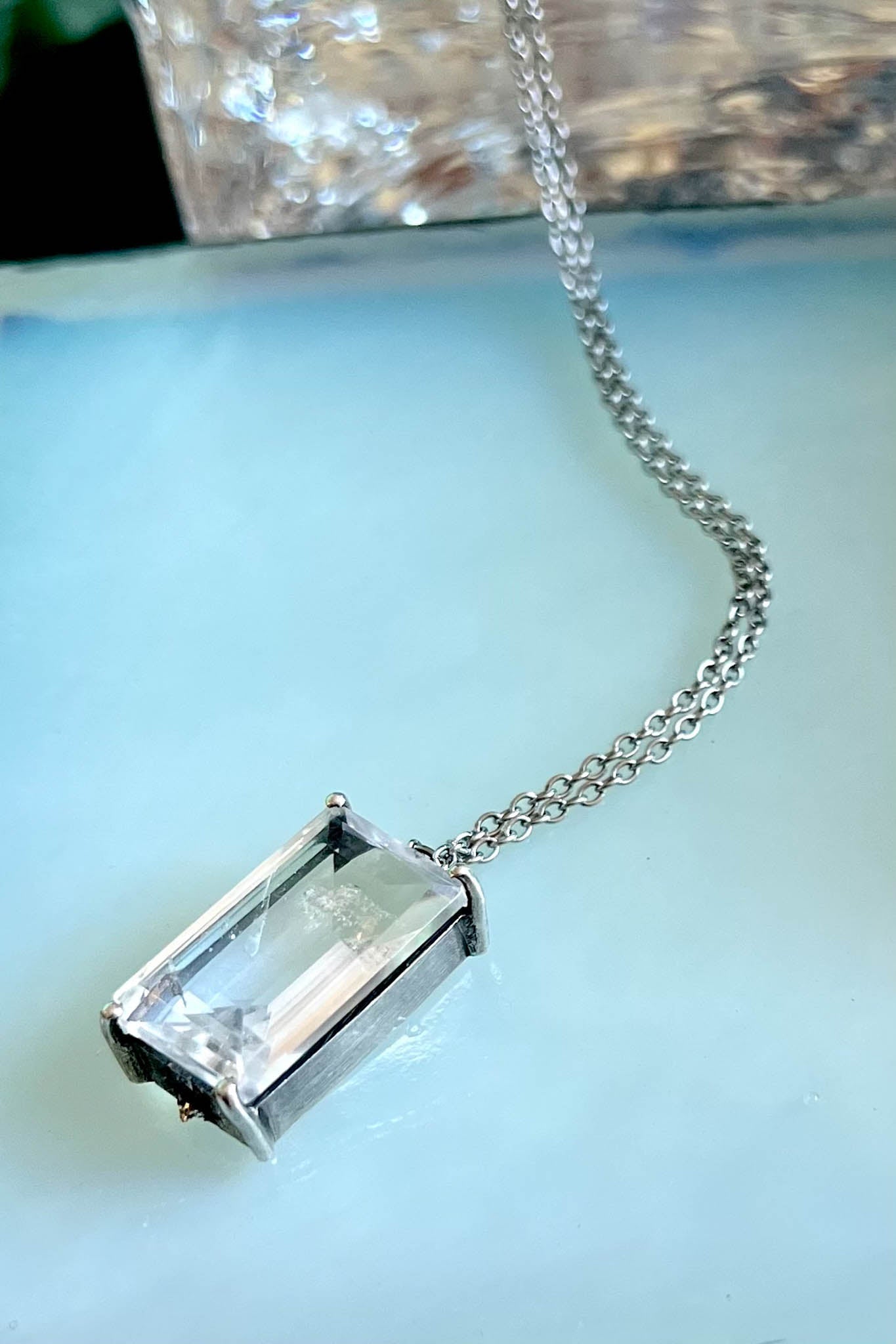 Silver necklace with a rectangular clear gemstone pendant on a light blue background