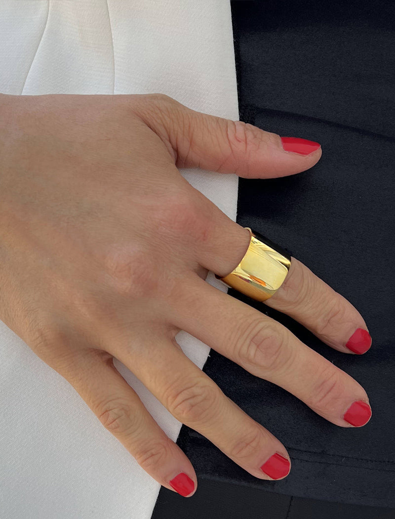 Hand wearing a gold ring with red nail polish on a black and white background