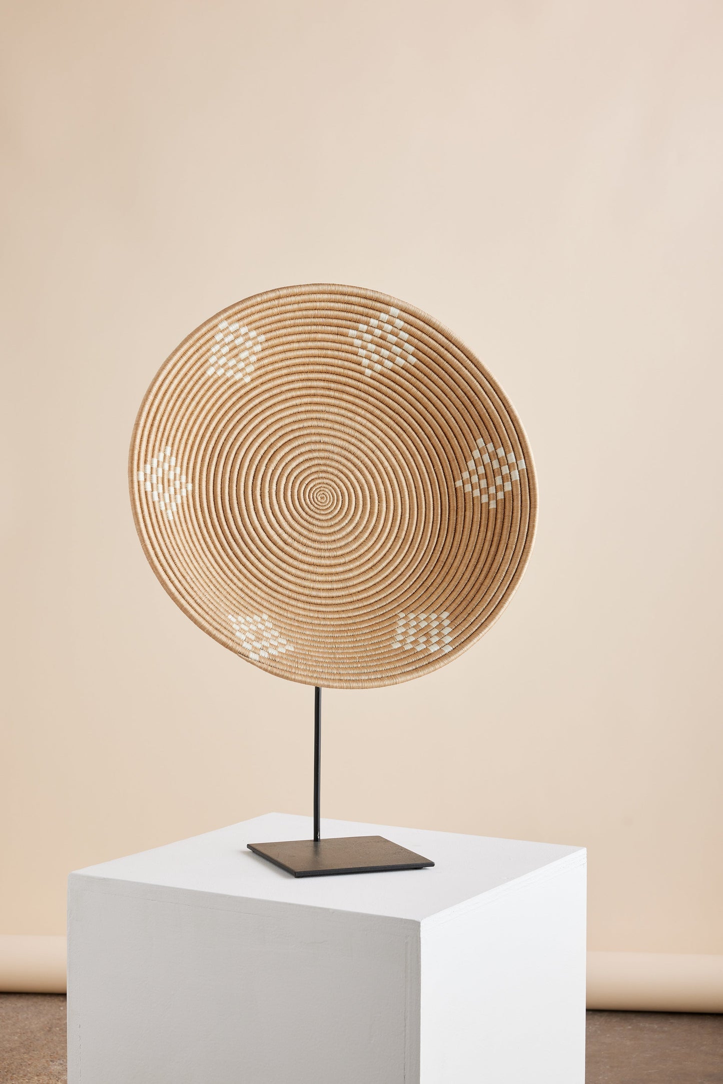 Decorative circular object on a white pedestal against a beige wall