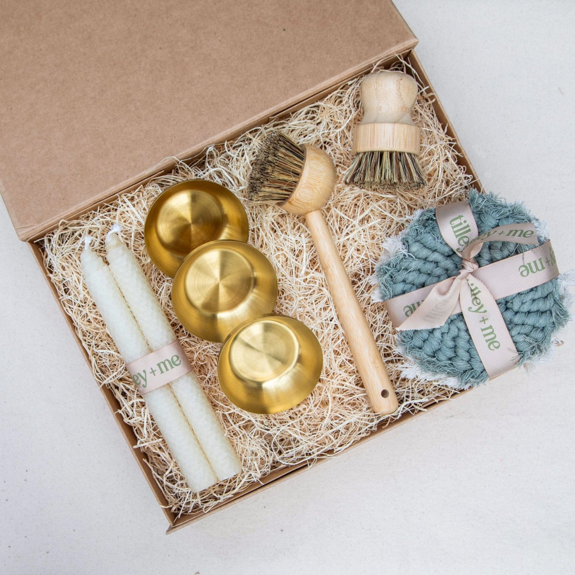Set of gold bowls, a brush, and a blue scrubber in a gift box on a white background