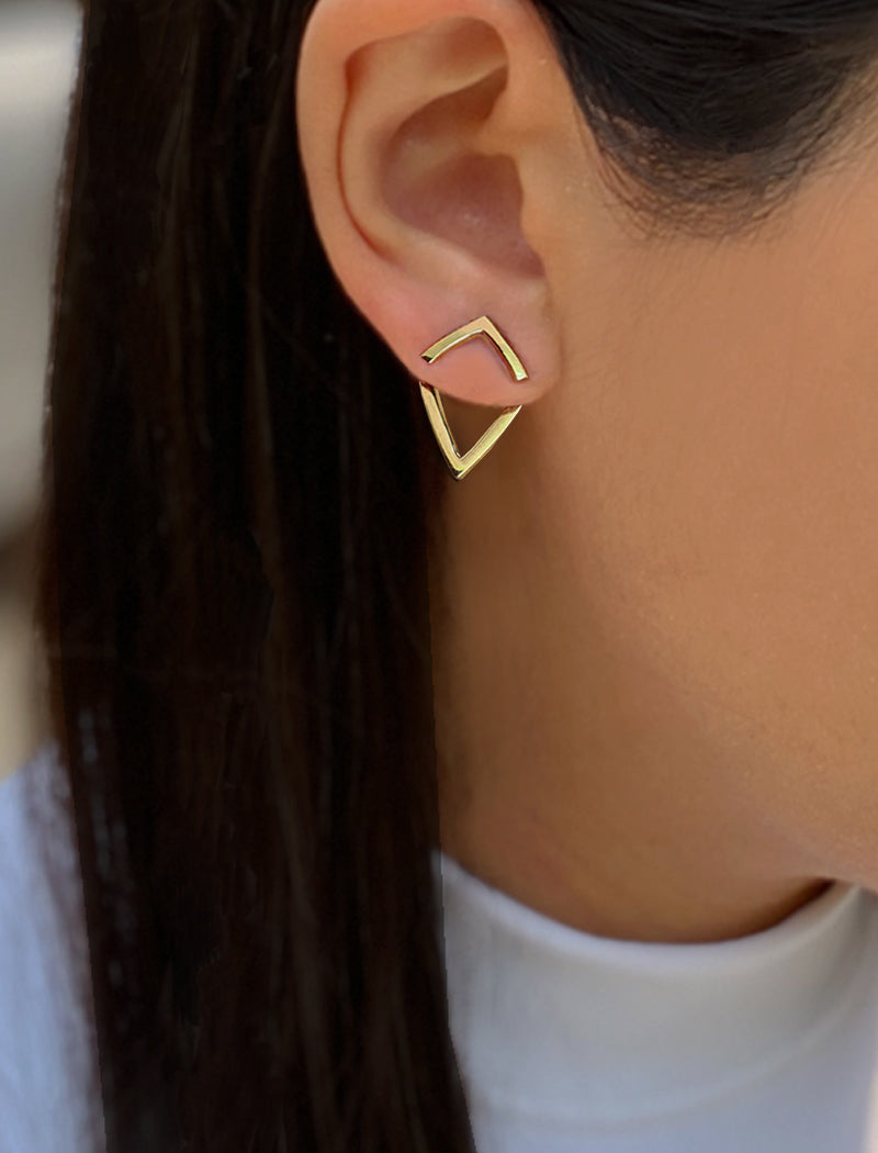 Gold geometric earring worn by a person with dark hair.