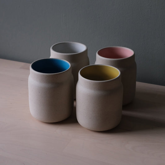 Four ceramic cups with colored interior finishes on a wooden surface.
