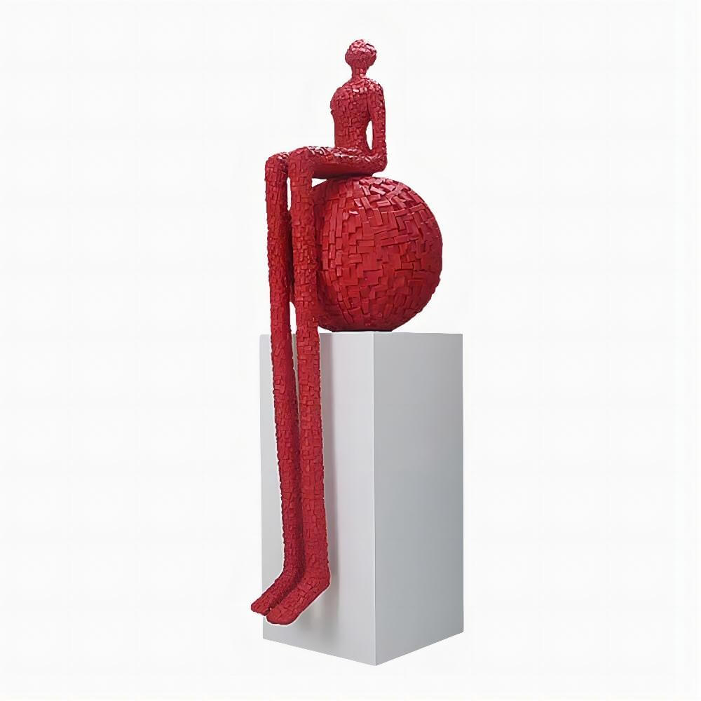 Red sculpture of a figure sitting on a ball on a white pedestal