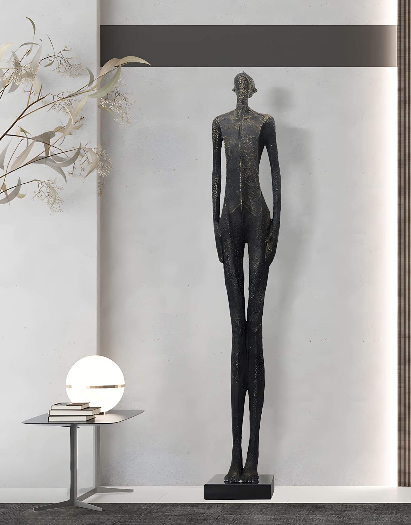 Tall black sculpture of a humanoid figure on a white wall background