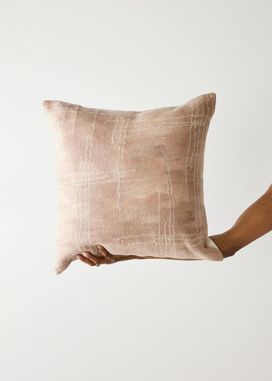 Hand holding a textured beige pillow against a plain background