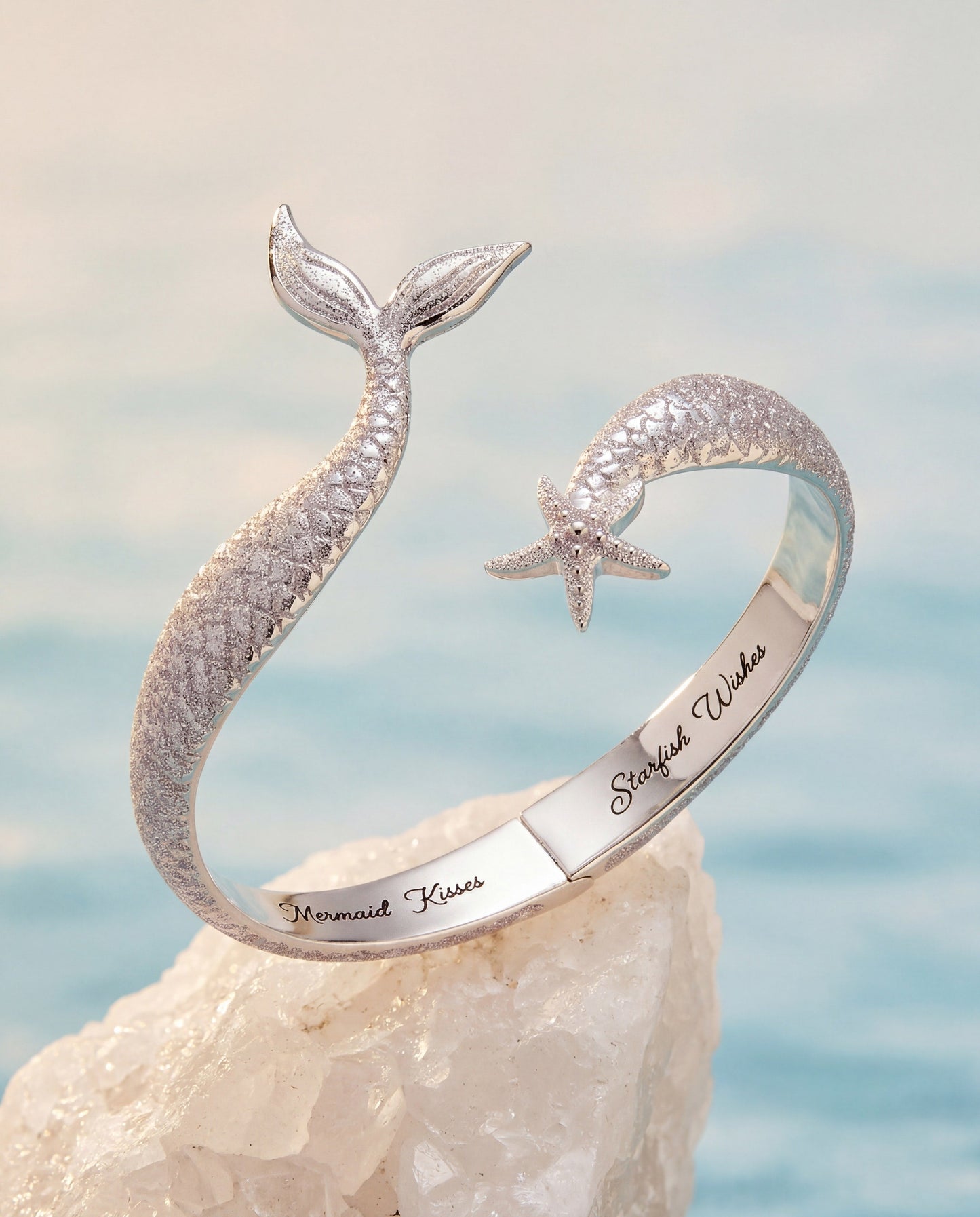 Silver mermaid tail bracelet with starfish charm on a rock with ocean background