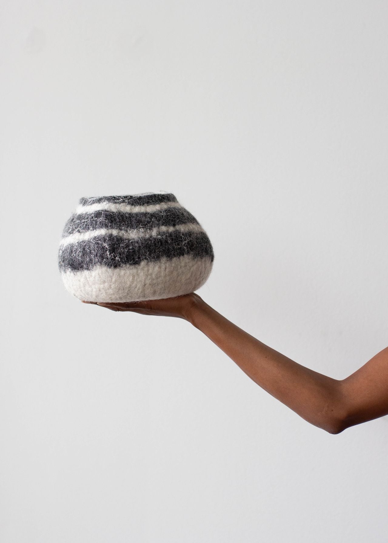 Hand holding a striped woven bowl against a plain background