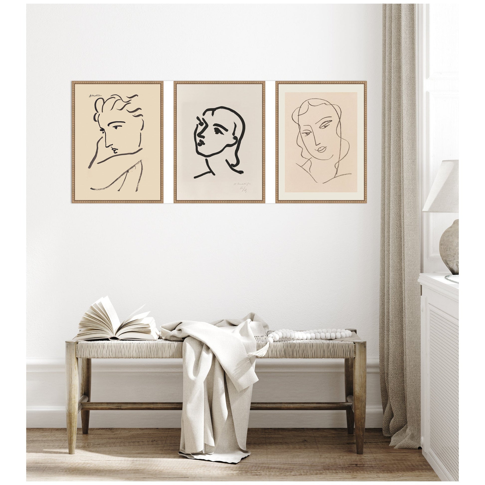 Three framed line art portraits on a wall above a bench with an open book and white blanket.
