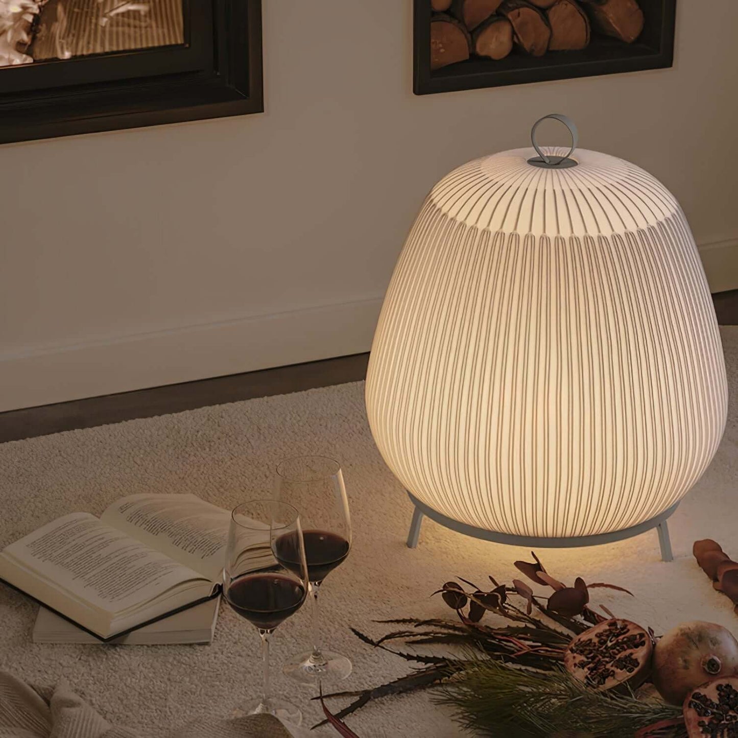Lamp on a table with a book, wine glasses, and decorative items in a cozy setting.