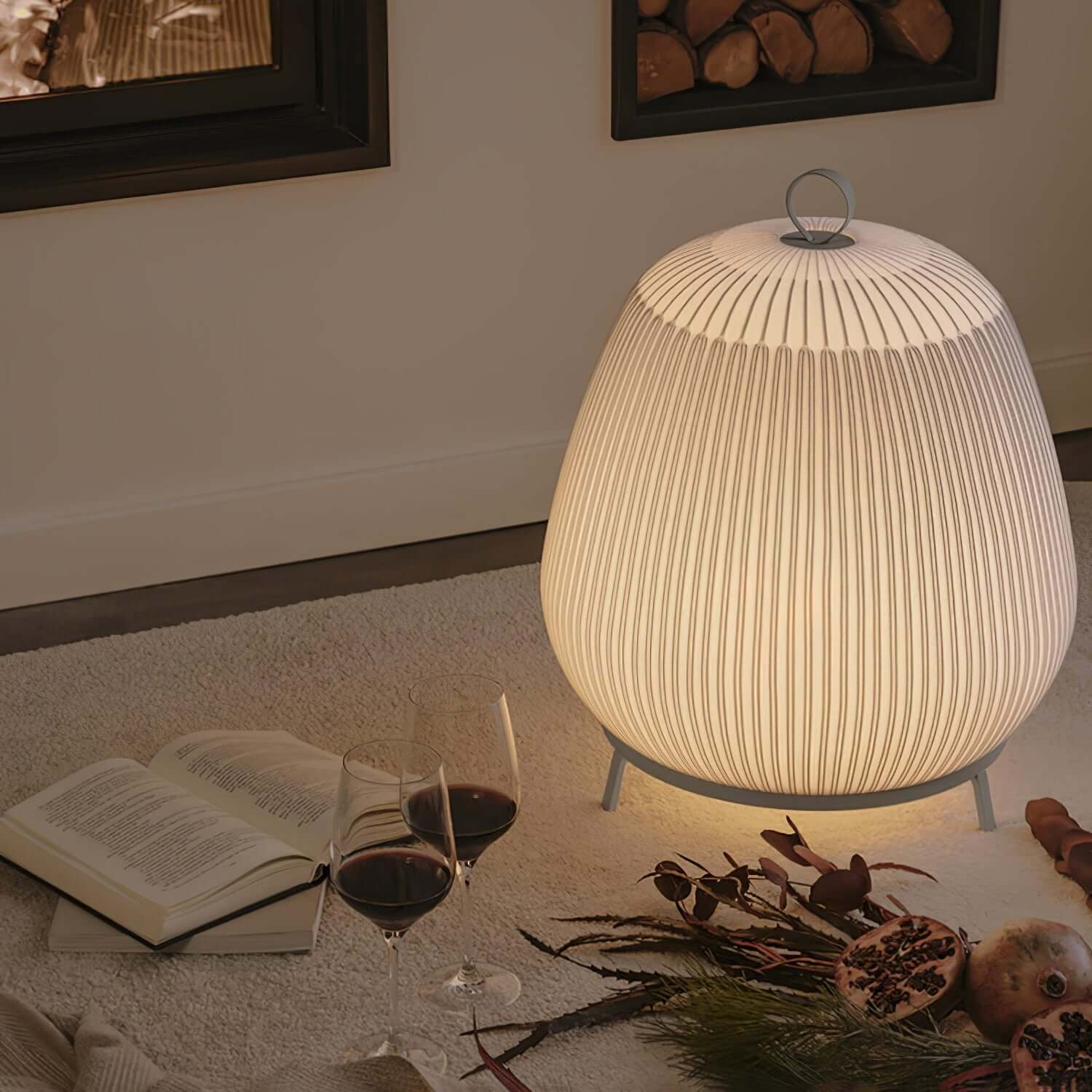 Lamp on a table with a book, wine glasses, and decorative items in a cozy setting.