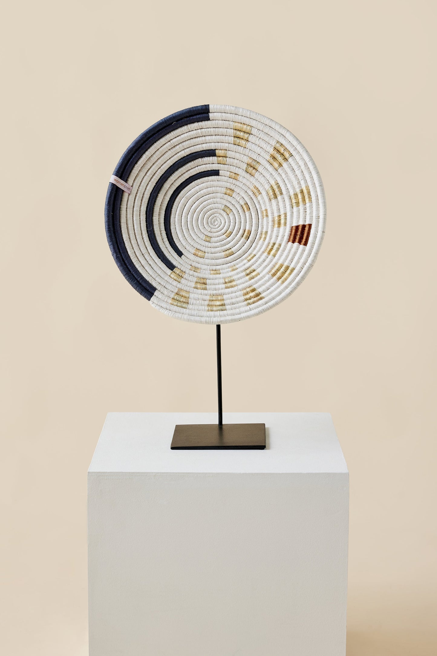 Decorative circular object with concentric patterns on a stand against a beige background