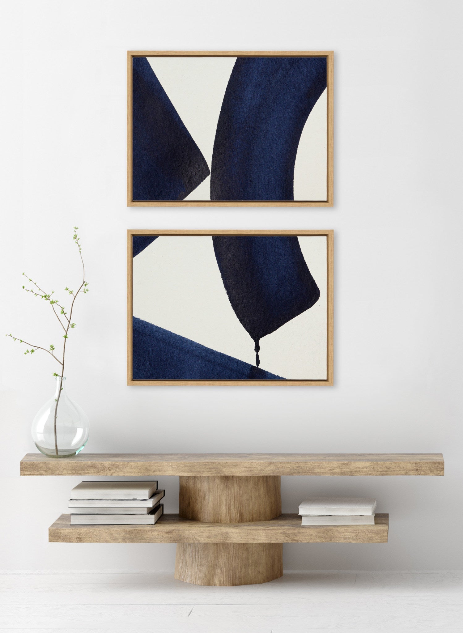 Two abstract artworks in wooden frames on a white wall above a wooden console table.
